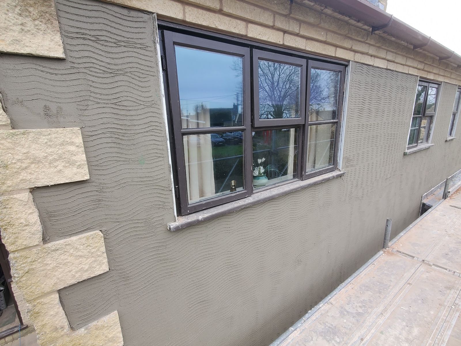 A combed render base coat on an exterior wall beside stone quoins