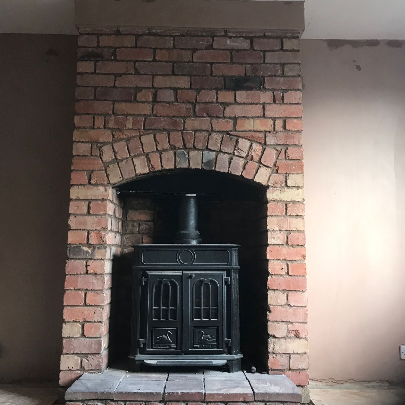 Freshly plastered walls either side of a brick fireplace with a wood burner